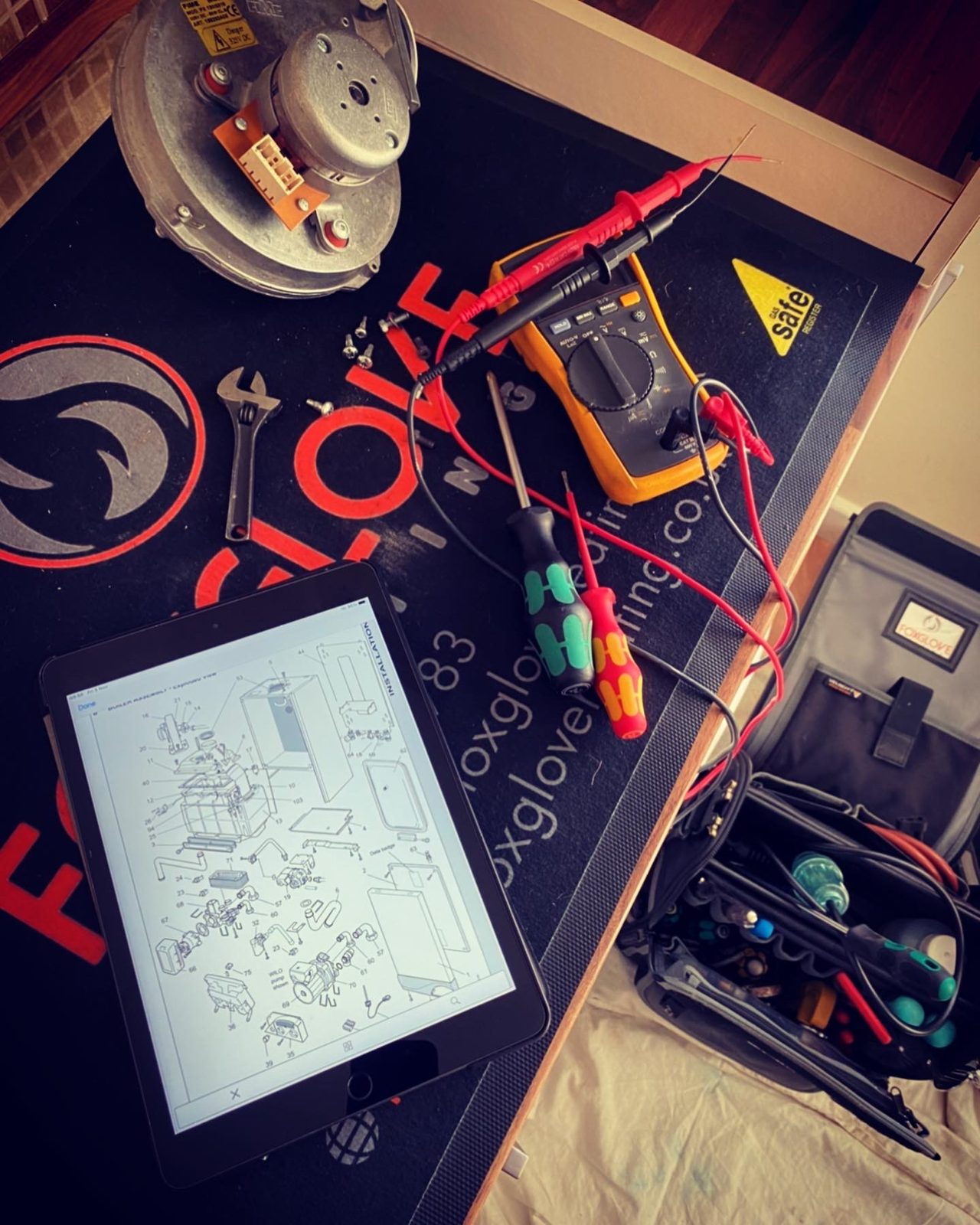 Fault-finding kit laid out on a Foxglove Heating mat: a multimeter, a tablet showing a wiring diagram and hand tools