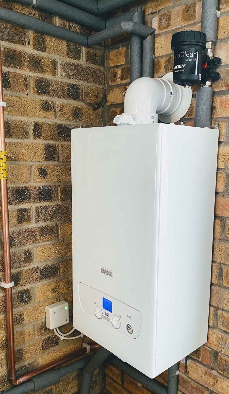 A new white Baxi combi boiler fitted on a brick wall with a grey flue
